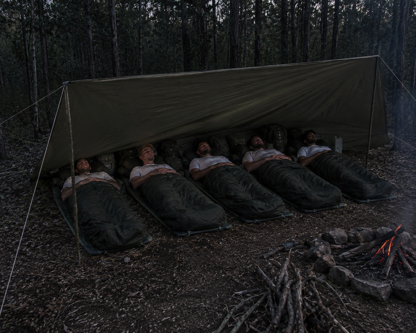 Participants sleeping in the field under a tarp shelter beside a campfire